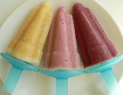 Three fruit ice lollies on a plate one yellow, one pink and one purple
