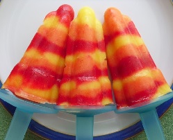 Three ice lollies made with thin stripes of red, yellow and orange fruit puree.